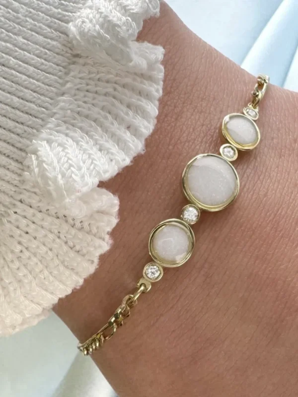 Breast milk keepsake bracelet with three round milk stones in gold bezels and diamond accents, worn on the wrist