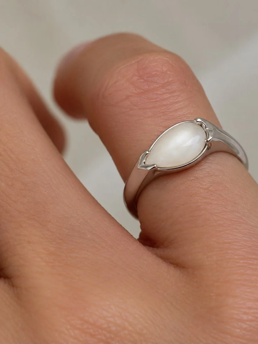 Breast milk keepsake signet ring with a pear-shaped milk stone, worn on the hand