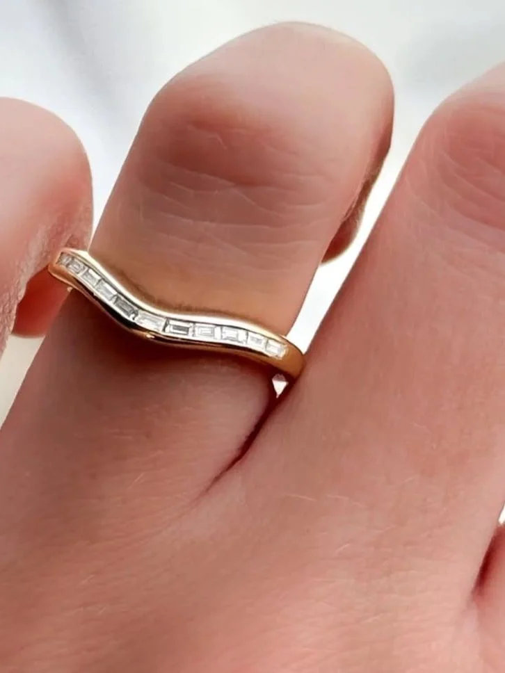 Curved chevron wedding band channel-set with baguette diamonds in gold, worn on the hand