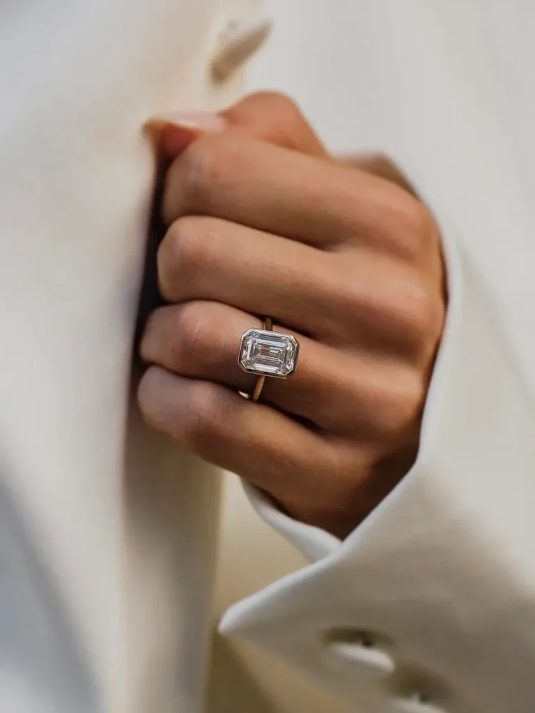 Emerald-cut diamond bezel solitaire ring in gold, worn on the hand